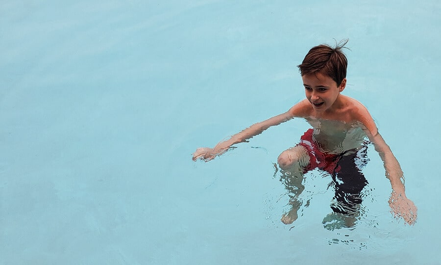 Menino de bermuda vermelha brincando na piscina. 