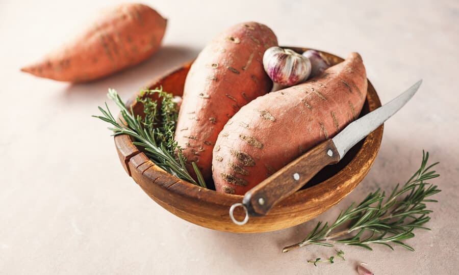 batatas doces em um cesto com uma faca e um ramo verde