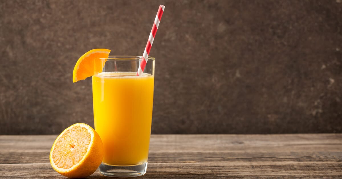 Copo com suco de laranja e um canudo colorido em cima da mesa.