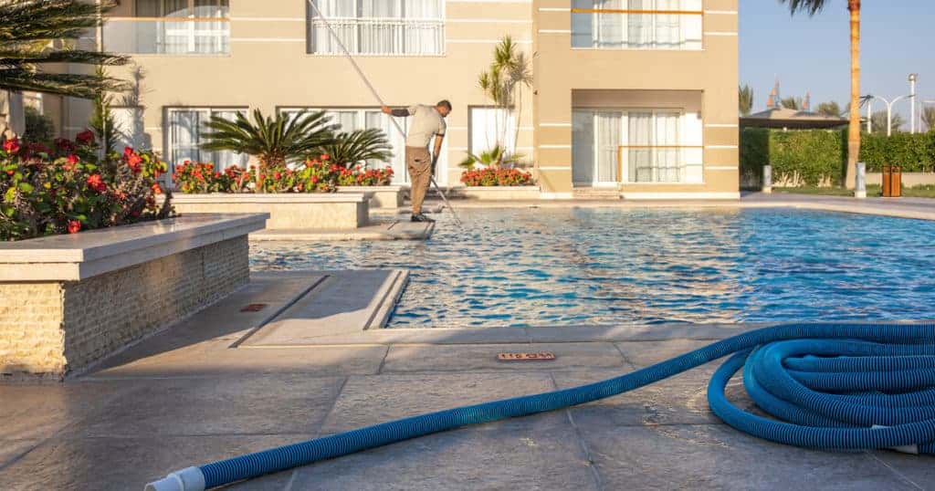 Homem limpando a piscina do prédio.