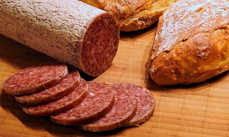 Salame italiano fatiado ao lado de dois pães.