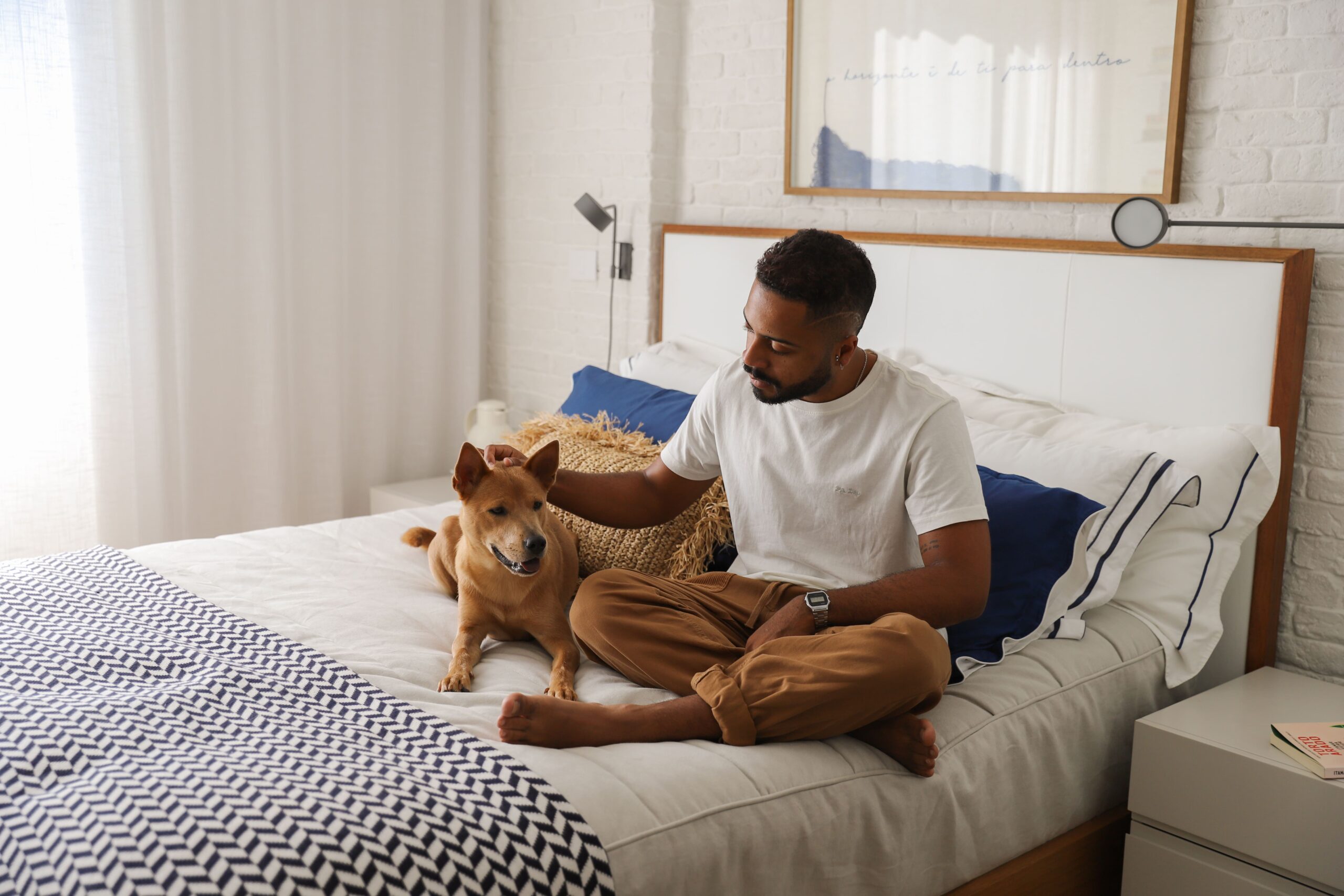 Tutor sentado na cama ao lado do cachorro.